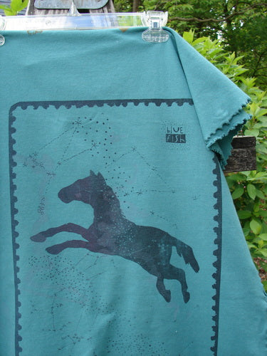 Barclay Heavy Weight Organic Sweatshirt Blanket Pony Garden Emerald OSFA, displayed outdoors, featuring a leaping horse silhouette with star-like patterns and a blue dish logo, clipped against lush foliage.