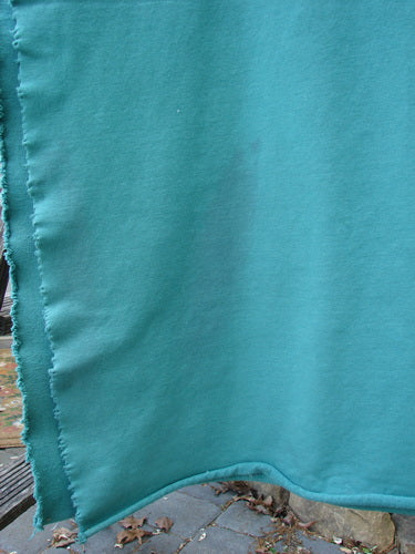 Barclay Heavy Weight Organic Sweatshirt Blanket Pony Garden Emerald OSFA draped outdoors, showcasing its versatile use with raw curly edges and floral designs, partially revealing paving stones and leaves beneath.
