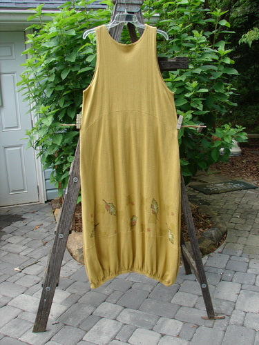 2000 Cotton Hemp Libby Jumper Falling Leaf Gold Altered Size 1, displayed hanging on a wooden ladder, showcasing its sophisticated drape, side pockets, and varying elastic hemline.