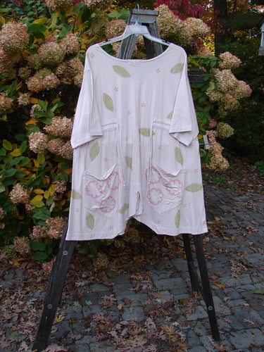 Barclay Double Draw Center Vent Tunic Top Leaf Pink Tile Size 2, featuring wide sleeves, a rounded neckline, two exterior pockets, and a flouncy lower skirt, displayed on a rack.