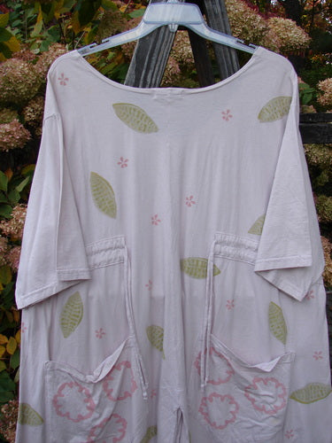 Barclay Double Draw Center Vent Tunic Top Leaf Pink Tile Size 2, featuring green leaf pattern, rounded neckline, wide sleeves, double rear drawcords, and a flouncy lower skirt on a hanger.