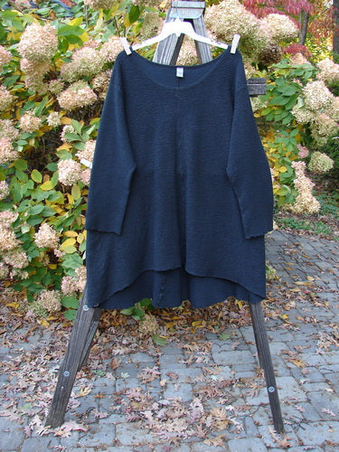 Barclay Crepe Hi Low Top Unpainted Black Size 2, displayed on a wooden rack, showcasing its textured stretch crepe fabric, wider rounded neckline, vertical center seam, and long cozy sleeves.