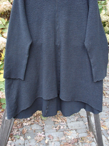 Barclay Crepe Hi Low Top Unpainted Black Size 2 displayed on a wooden stand, showcasing its textured stretch crepe fabric, wider rounded neckline, long sleeves, and upward curved front hemline.