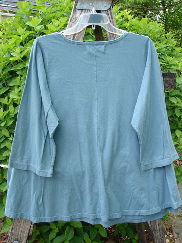 Barclay Three Quarter Sleeved A Lined Tee Creativity Everyday Dusty Sky Size 0, featuring a loose fit and sweet curly edgings, displayed on a hanger outdoors against a backdrop of greenery.