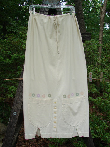 2001 Wishpocket Skirt Circle Rows Natural Size 1, displayed on a wooden ladder, featuring two oversized lower pockets, a half-drawstring waist, and six vertical hem buttons.