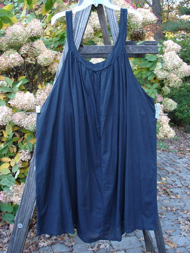 Barclay Batiste Banded Collar Slip Dress Unpainted Black Size 2 displayed on a wooden structure, showcasing deep neckline, gathered fabric, and wide swingy lower hemline.
