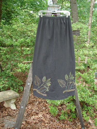 1998 Botanicals Corolla Skirt Leaf Vine Raven Size 1 displayed on a wooden stand, featuring an upward scooped front hemline with a leaf vine pattern, full elastic waistband, and no pockets.