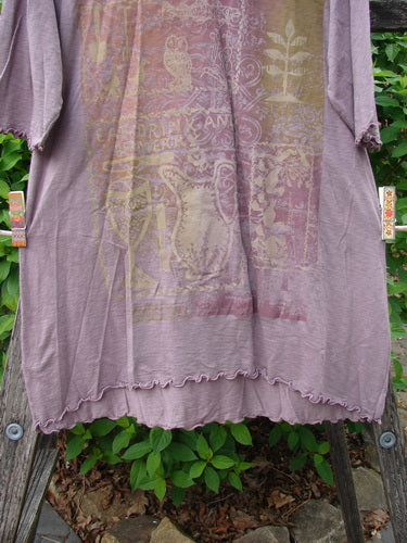 Barclay Slub Modal Three Quarter Sleeved Cafe Tee Merry Farm Mallow Size 0 features a loose fit, ornate owl graphic, and curly-edged, three-quarter sleeves, displayed on a wooden rack amid foliage.