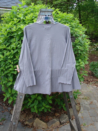 Barclay Long Sleeved Cafe Tee Poetry Garden Grey Day Size 0 on a wire hanger, highlighting its A-line shape, rounded neckline, and curly edging, set against a natural outdoor background.