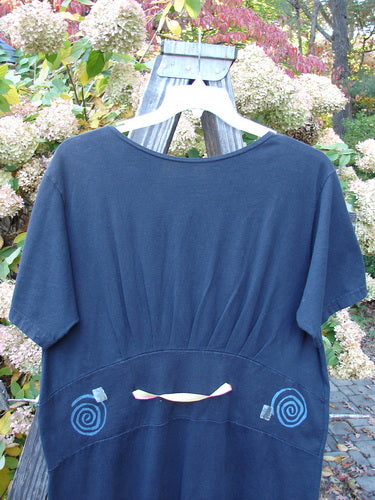 1992 Little Storma Dress Garden Bug Black Small OSFA hanging on a wooden rack, showcasing its unique design with a deep rounded neckline, tapered lower, gathered back, and signature Blue Fish Vintage Patch.