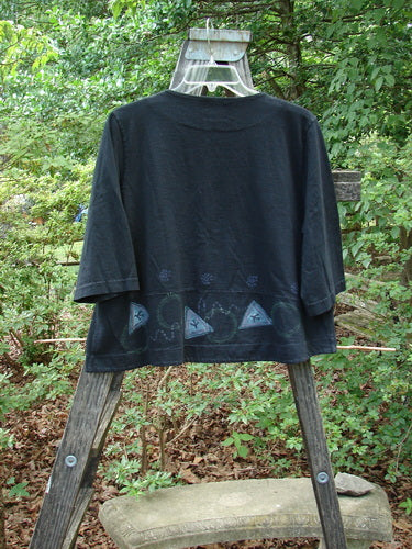 2000 4 Corners Jacket Travel Stone Black Size 1, featuring a cropped flared shape, floral blue buttons, and a double-paneled hem, displayed outdoors on a hanger.