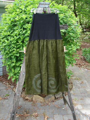 2000 Silk Organza Aios Dana Skirt Celtic Lichen Size 1, featuring a black lycra upper and olive-green lower with subtle spiral motifs, elegantly displayed on a wooden ladder outdoors.