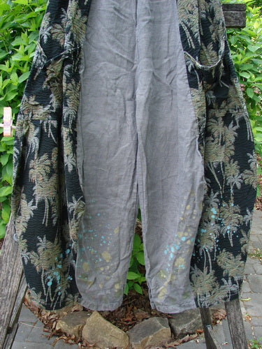 Barclay Linen Pucker Accent 4 Square Pant Tropical Black Grey Size 0 draped over a garden bench, showcasing light-grey linen with faint yellowish and turquoise paint splatters along the lower legs.