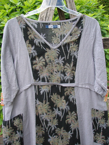 Barclay Linen Pucker Heart and Soul Dress Tropical Black Grey Size 0 hangs outdoors, showcasing its black palm motif, contrasting light gray sleeves, deep V-neckline, and unique textures, framed by green foliage.
