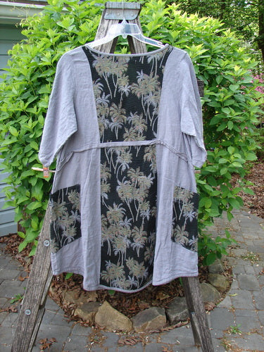 Barclay Linen Pucker Heart and Soul Dress Tropical Black Grey Size 0, featuring a loose fit, gray body with palm-motif panels, three-quarter sleeves, and boxy patch pockets, hanging on a wooden ladder.