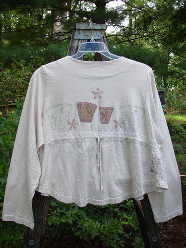 1999 Coffee Top Flowerpot Tea Dye Size 1: White shirt with a flower design, featuring a rounded hemline, big button closures, and a drawcord back, made from organic cotton.
