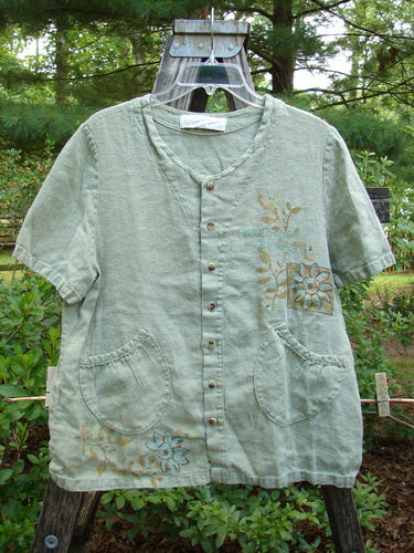 1998 Botanicals Robin's Top Daisy Elm Size 0 displayed on a hanger, featuring a daisy and garden theme, dual front pockets, and 7 buttons, made from heavyweight linen.