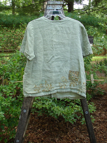 1998 Botanicals Robin's Top Daisy Elm Size 0 displayed on a wooden rack, featuring dual front elastic pockets, a super A-line shape, and daisy-themed paint on heavyweight linen.