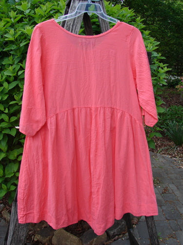 Barclay Linen Two Pocket Dolly Dress Notes Coral Size 0, featuring a flouncy lower skirt, dropped empire waist, and dual exterior drop pockets, hanging against a garden backdrop.