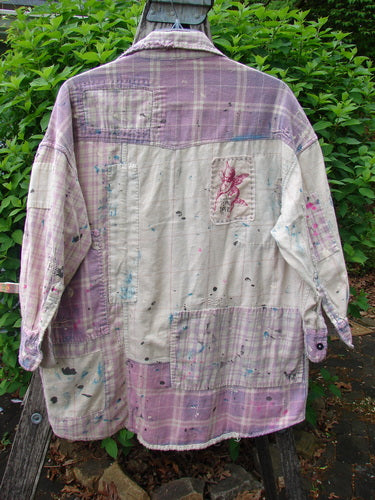 Magnolia Pearl Flannel Patched Surfside Shirt Sun Bleached OSFA, a long-sleeved shacket with purple-and-cream plaid, distinctive paint splatters, and generous patchwork, displayed outdoors draped over a wooden frame.