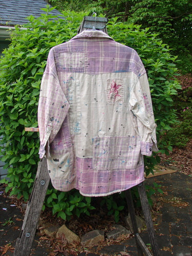 Magnolia Pearl Flannel Patched Surfside Shirt Sun Bleached OSFA, featuring patchwork panels, paint splatters, and an embroidered motif, displayed outdoors on a wooden ladder against a green shrub backdrop.