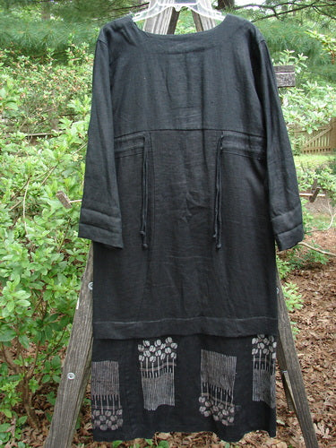 2000 Ringlet Dress Tulip Grass Black Altered Size 1, displayed on a wooden rack, featuring white daisy patterns, oversized pockets, and a rounded V-neckline.