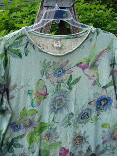 Magnolia Pearl Cotton Jersey Boyfriend Tee Passion Flower Big Sky OSFA features vibrant nature motifs with hummingbirds and butterflies, showcasing rolled edges and shoulder distressing on soft cotton, hanging outdoors on a clear hanger.