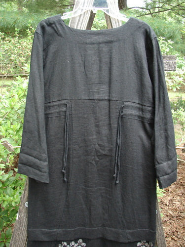 2000 Ringlet Dress Tulip Grass Black Altered Size 1 displayed on a clothes rack, showcasing its oversized pockets, sectional panels, and unique V-shaped neckline, with a daisy-themed continuous hem.