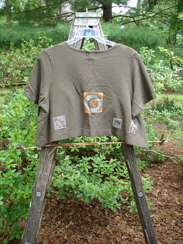 2000 Patched Recycle Jacket Science Bark Size 0 displayed on a wooden swing, showcasing its wide, flared hemline, rounded neckline, drop pocket, and colorful bio-themed patches.