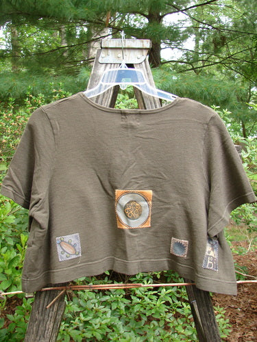 2000 Patched Recycle Jacket Science Bark Size 0 displayed on a hanger, featuring a rounded neckline, flared hem, front squared drop pocket, and various colorful patches in a bio theme.