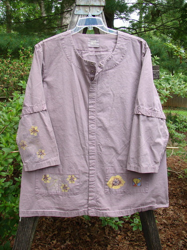 2000 Parachute Camper Jacket Florals Pale Purple Size 0 featuring yellow floral designs, versatile snap buttons, and four painted front pockets, displayed against an outdoor background.