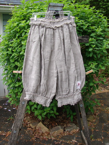 Magnolia Pearl Homespun Linen Crop Smocked Bloomer Flaxen OSFA displayed on a hanger over a wooden ladder, showcasing its elasticized waist, smocked cuffs, and signature patches, embodying Bluefishfinder's vintage style.