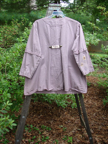 2000 Parachute Camper Jacket in Pale Purple, displayed on a wooden stand, featuring floral painted pockets, snap-off sleeves, and a snap front line. Rare vintage piece from Bluefishfinder.com.