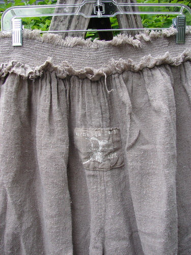 Magnolia Pearl Homespun Linen Crop Smocked Bloomer hangs outdoors, showcasing its gathered elastic waistband, small front patch pocket, and raw-edged smocking, reflecting Bluefishfinder.com's vintage, creative fashion ethos.