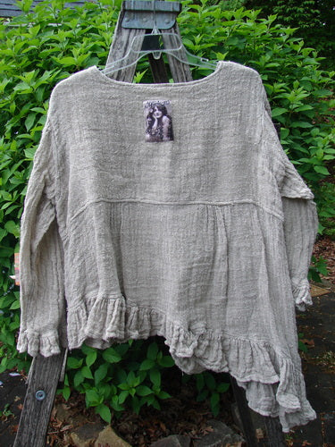 Magnolia Pearl Fisherman's Weave Asymmetrical Ruffle Jacket OSFA draped over a wooden ladder, features textured natural-fiber fabric, ruffled hems, oversized pearl buttons, and a vintage patch, embodying Bluefishfinder.com's creative individuality.
