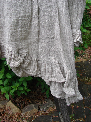 Magnolia Pearl Fisherman's Weave Asymmetrical Ruffle Jacket OSFA draped over wood, showcasing its loosely woven texture, dramatic asymmetrical ruffled hemline, oversized pearl buttons, and sweet lower sleeve ruffles.