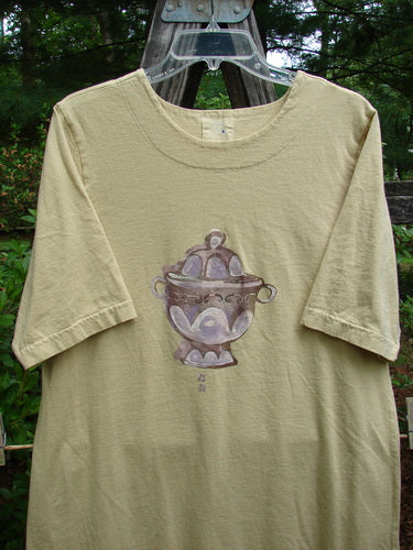1999 Straight Dress Sugar Bowl Plantain Altered Size 1: Tan shirt with Sugar Bowl-themed painting, rounded neckline, two side pockets, seamless front, widening hips, narrowing vented hemline, and Blue Fish Patch.
