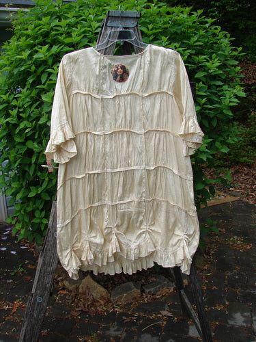 Magnolia Pearl Silk Cotton Drapery Dress Butter Creme OSFA hangs outdoors, showcasing its cream color, fluttery sleeves, ruffled tiers, and bow details, embodying vintage elegance and comfort.