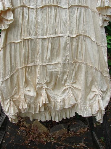 Magnolia Pearl Silk Cotton Drapery Dress Butter Creme OSFA features ruffled tiers, vertical pleating, and a full ruffled hemline, showcasing elegant craftsmanship in a lightweight, delicate fabric.