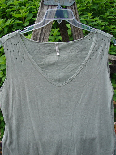 Magnolia Pearl Cotton Jersey Vented Layer Tank Top Green River OSFA displayed on a clear hanger over a wooden ladder, featuring raw flutter edges, vented sides, and signature distressing, against leafy backdrop.