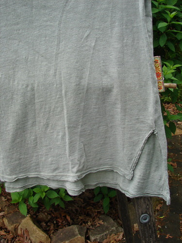 Magnolia Pearl Cotton Jersey Vented Layer Tank Top Green River OSFA displayed outdoors, features a light-gray knit with an uneven hem, side slit, and raw edges, draped gracefully over a wooden post.