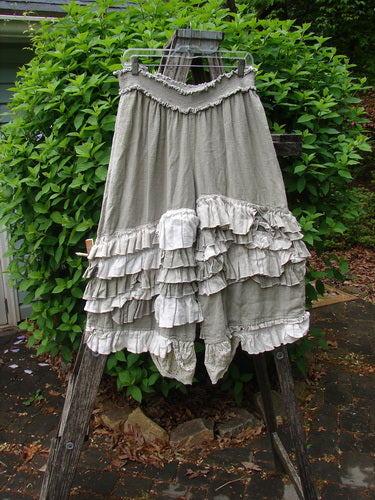 Magnolia Pearl Linen Eiffel Tower Bloomer Flaxen OSFA, featuring tiered ruffles and smocked waist, draped on a wooden ladder against a garden backdrop, highlighting its unique shape and texture.