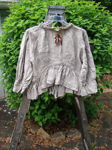 Magnolia Pearl Homespun Linen Snap Jacket Flaxen OSFA displayed on a rustic stepladder, showcasing its gathered waist, ruffled neckline, and flouncy hem, embodying vintage elegance and creative freedom.