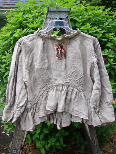 Magnolia Pearl Homespun Linen Snap Jacket Flaxen OSFA displayed draped over a wooden ladder, showcasing its ruffled neckline, snap front, and tiered hem, highlighting Bluefishfinder.com's vintage-inspired, creative fashion.
