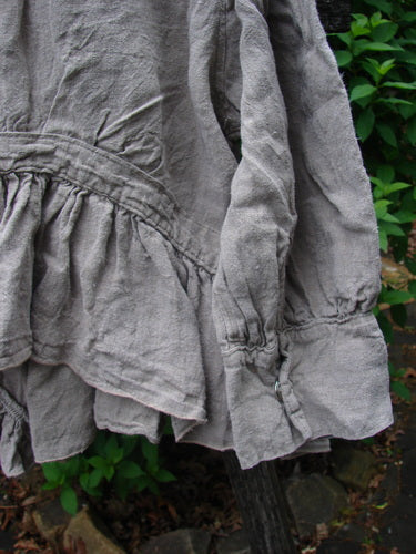 Magnolia Pearl Homespun Linen Snap Jacket Flaxen OSFA features a peplum waist, ruffled neckline, and cuffs. Textured heavy linen hangs against greenery, highlighting its vintage-inspired style from Bluefishfinder.com.