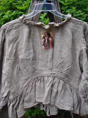 Magnolia Pearl Homespun Linen Snap Jacket Flaxen OSFA features a ruffled neckline, snap closure, and peplum hem. Displayed on a hanger, this vintage-inspired piece embodies Bluefishfinder.com's unique and expressive style.