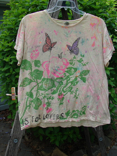 Magnolia Pearl Cotton Jersey Boyfriend Tee … Is For Lovers OSFA features a green rose and butterfly print on pale tie-dye fabric, displayed on a hanger against greenery, highlighting its artistic, vintage style.