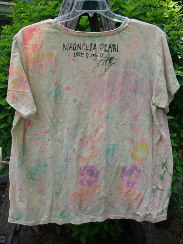 Magnolia Pearl Cotton Jersey Boyfriend Tee adorned with pastel floral motifs and LOVE SUPPLY CO lettering, hangs outdoors. It features a distressed, artistic design with a watercolor-like finish.
