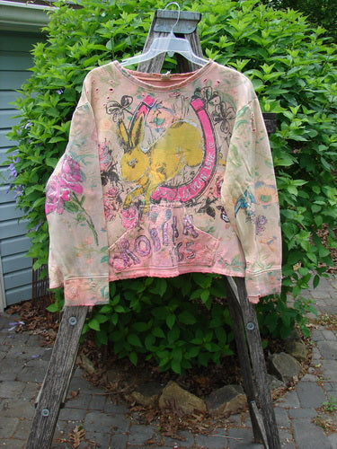 Magnolia Pearl Fleece Lucky Anna Glitter Sweatshirt Marais OSFA features a hand-painted, tie-dyed design with a large yellow bunny graphic, floral doodles, and glitter accents, hanging outdoors on a wooden ladder.