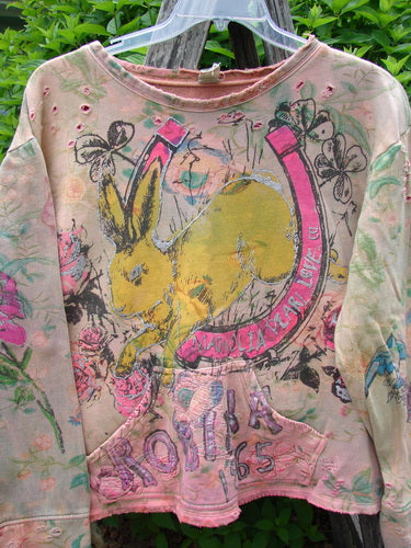 Magnolia Pearl Fleece Lucky Anna Glitter Sweatshirt Marais OSFA features a yellow rabbit graphic within a pink horseshoe, surrounded by flowers and butterflies, on a light pink distressed pullover with a kangaroo pocket.